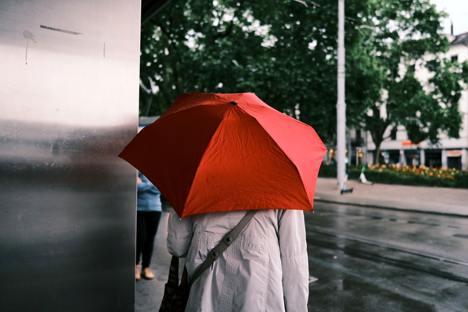 Zurich rain outfit with red umbrella and light coat on wet city pavement
