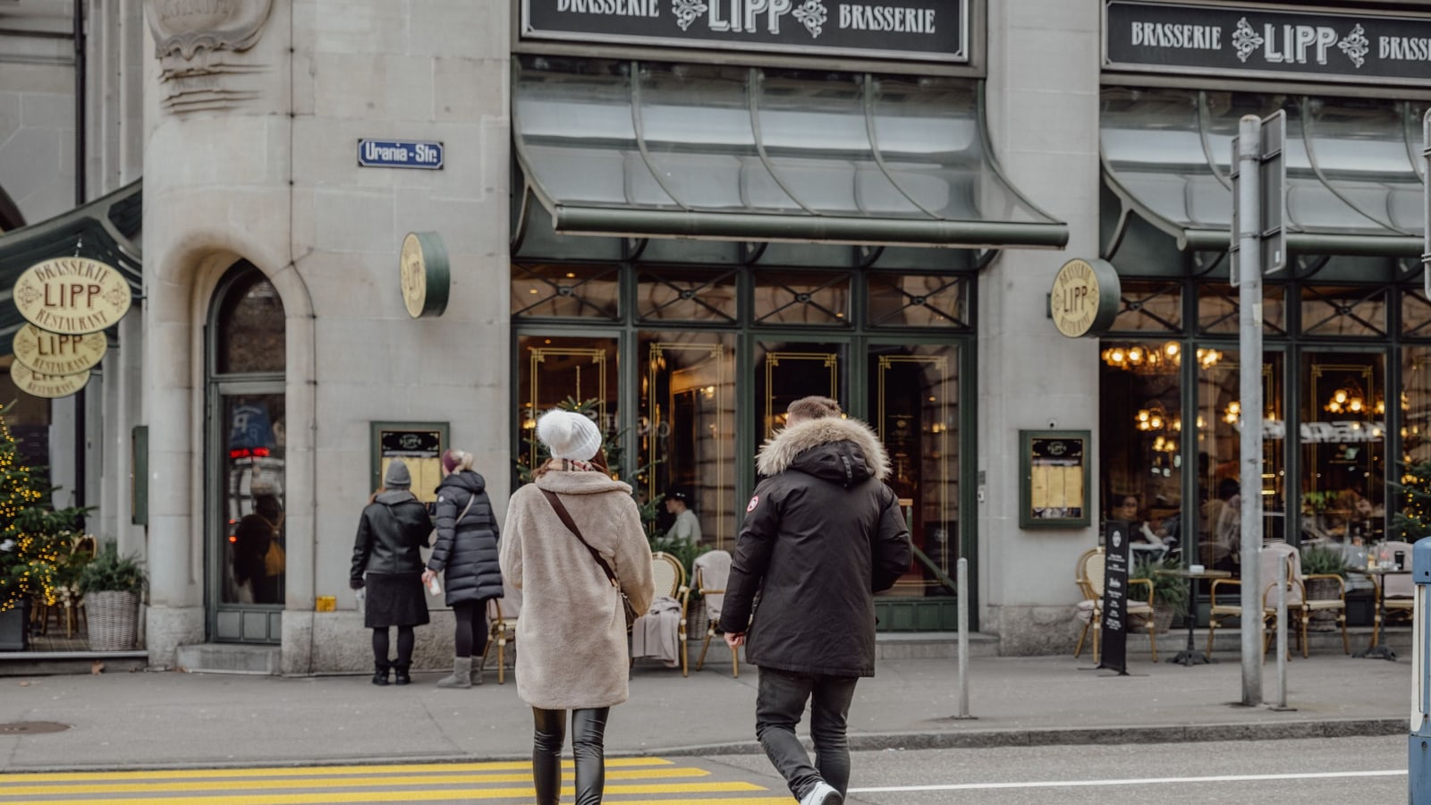 Zurich winter coat street style with a beige coat and black parka crossing near Brasserie Lipp