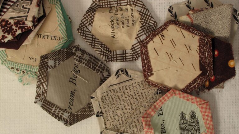 Hexagonal patchwork fabric pieces cut from used cloth and pinned to paper templates