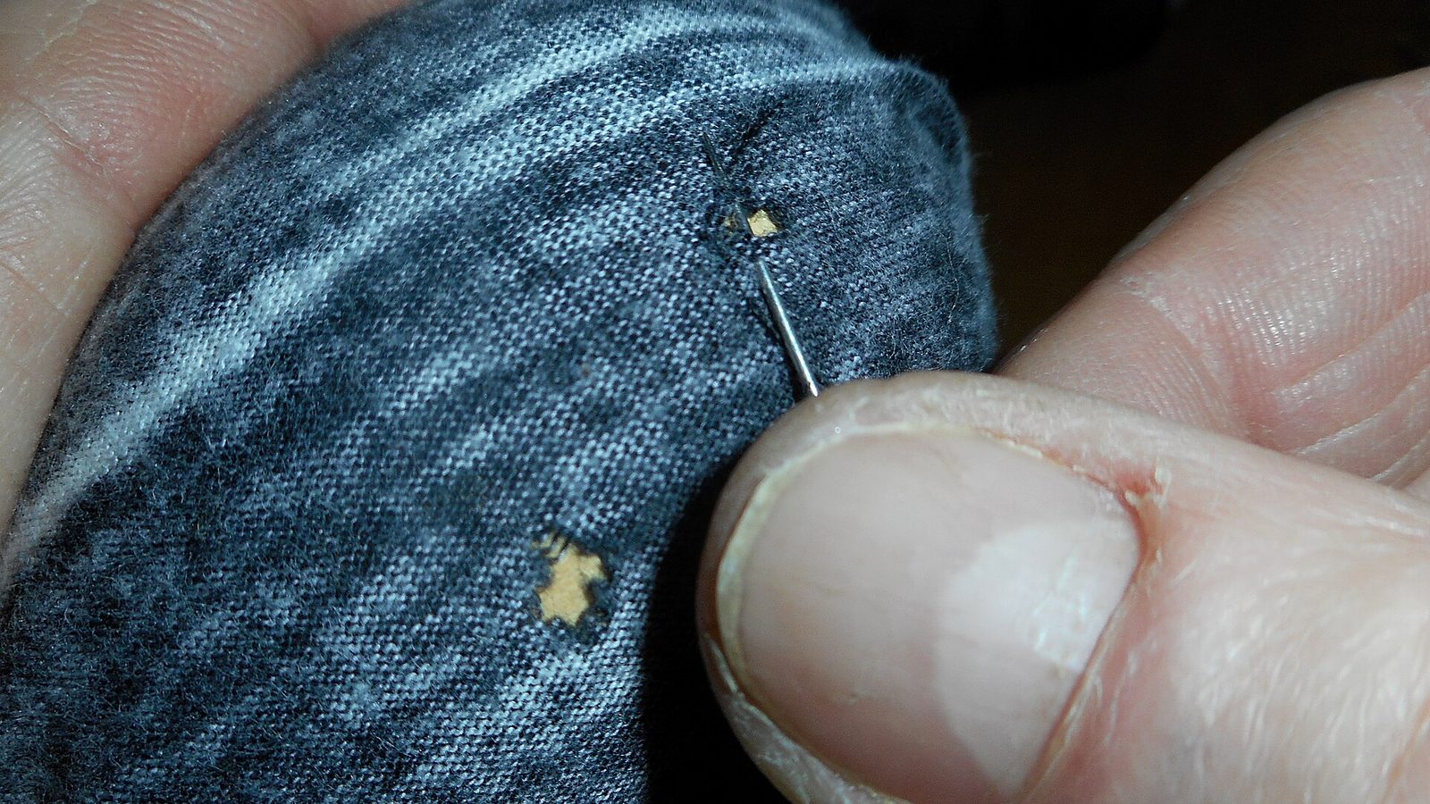 Darning a small hole in a knitted garment with needle and thread